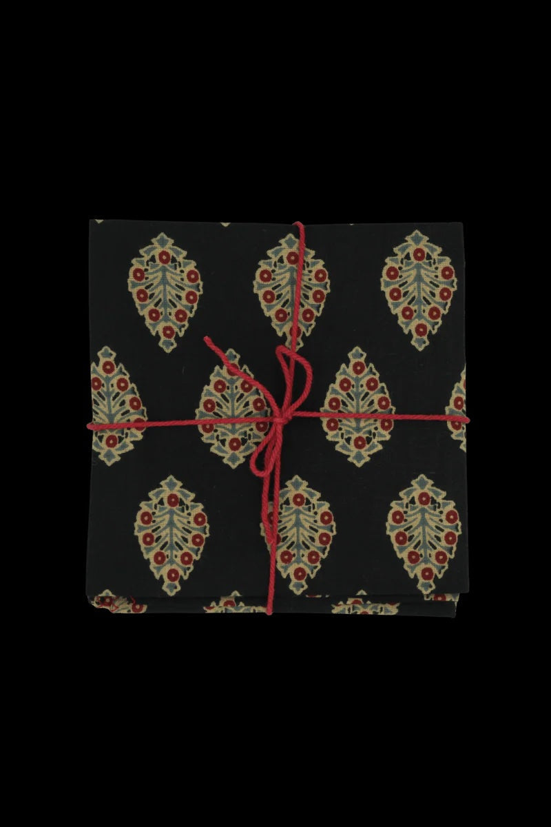 A black napkin set with floral pattern tied with a red string on a dark background ©Sprout Home