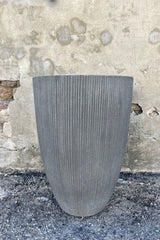 Photo of dark gray ficostone Ben pot outdoor planter with vertical ridged texture against a cement wall.
