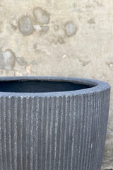 Close Photo of dark gray ficostone Ben pot outdoor planter with vertical ridged texture against a cement wall.