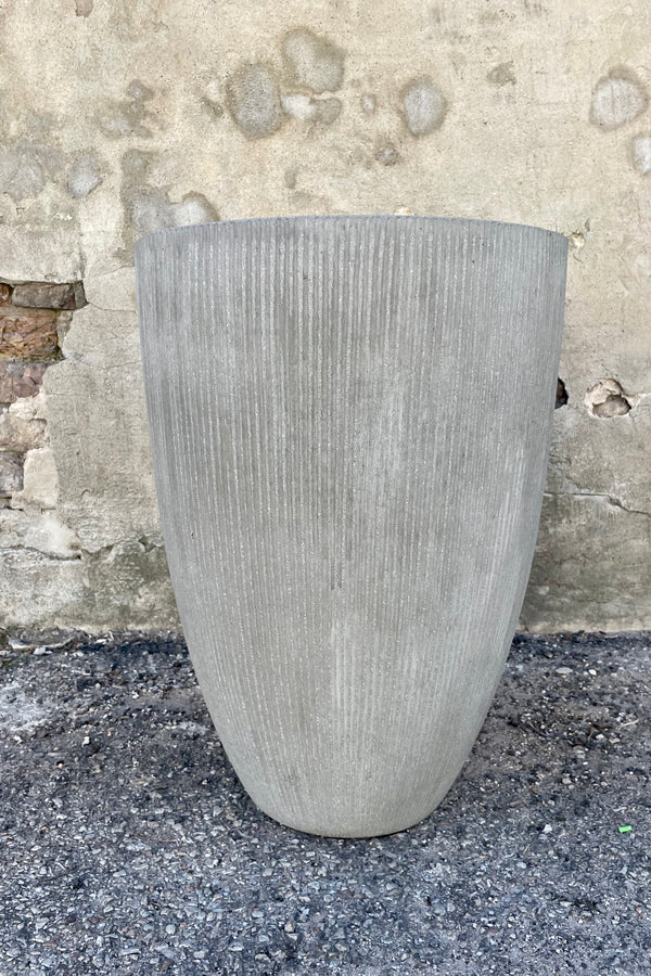 Photo of light gray ficostone Ben pot outdoor planter with vertical ridged texture against a cement wall.