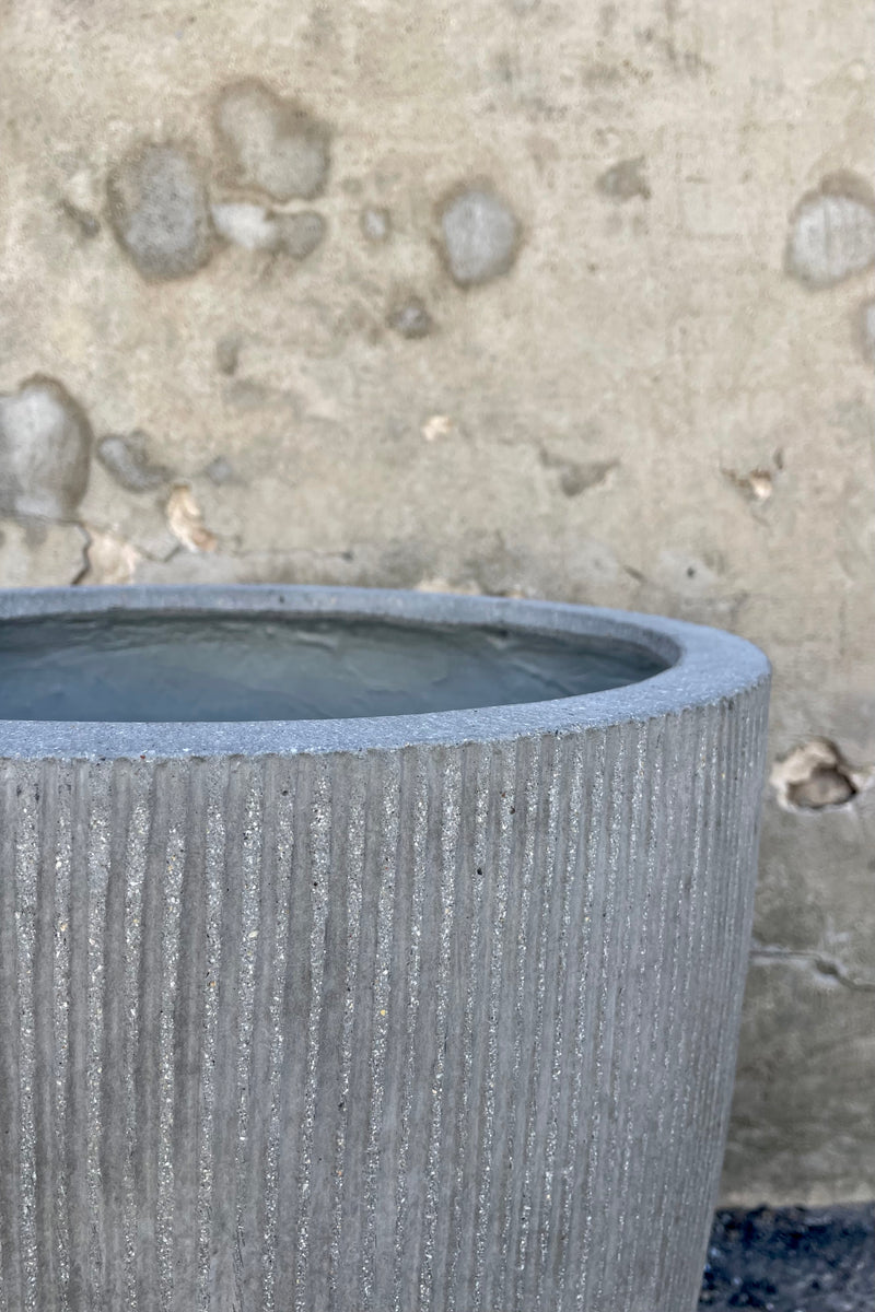 Close Photo of light gray ficostone Ben pot outdoor planter with vertical ridged texture against a cement wall.