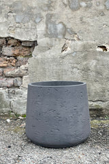 Photo of extra extra large Patt Pot planter with textured matte black finish against a cement wall.