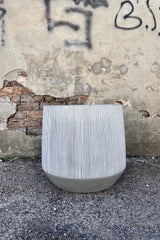 Photo of white and gray striped Harith pot against a cement wall.