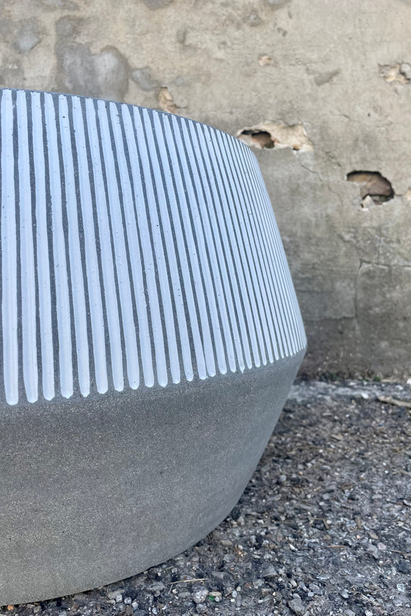 Photo of the angled side of white and gray striped Harley Low Pot against a cement wall.