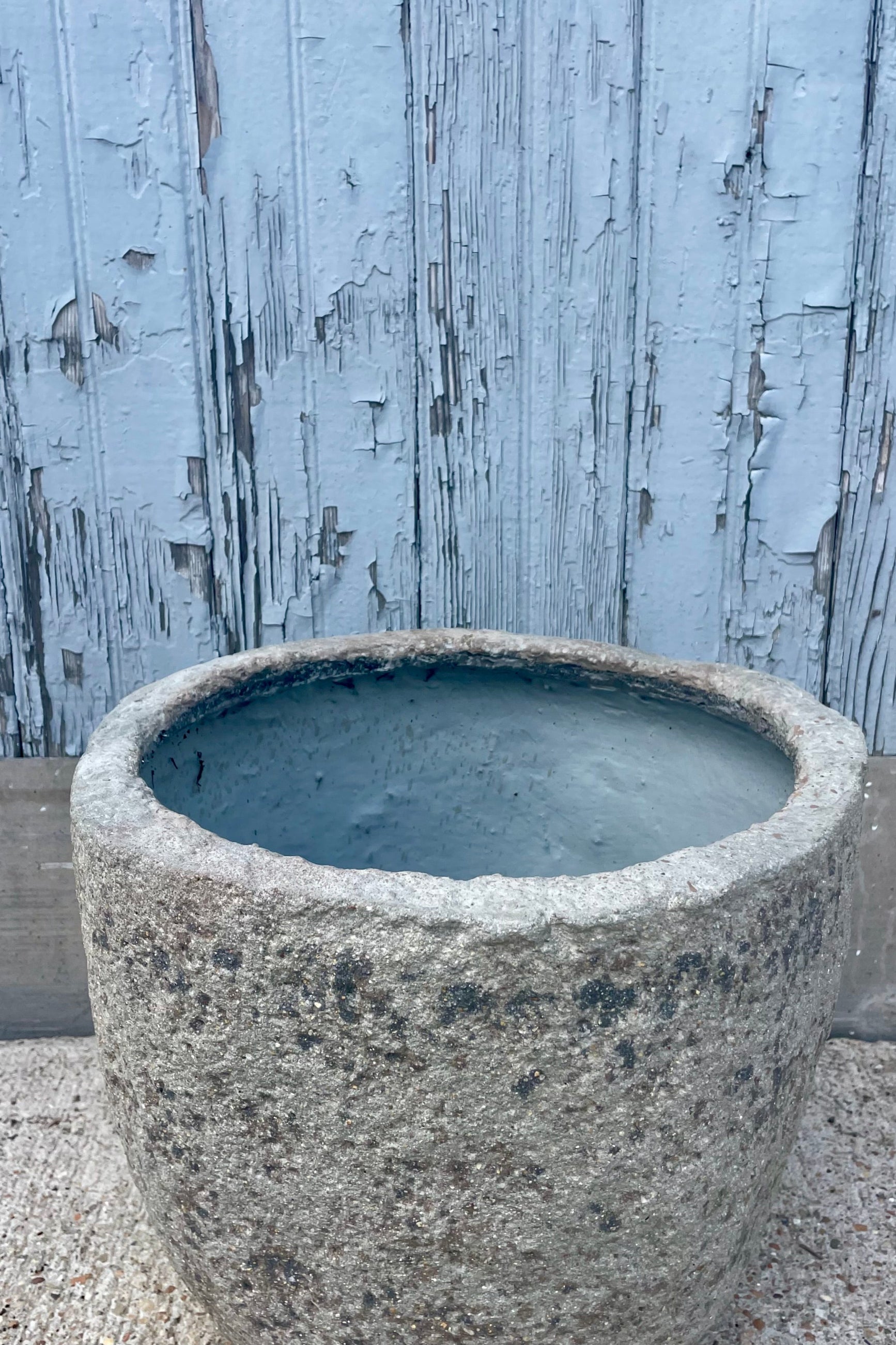 Close photo showing the side and interior opening of a textured gray pot in front of a wooden wall ©Sprout Home
