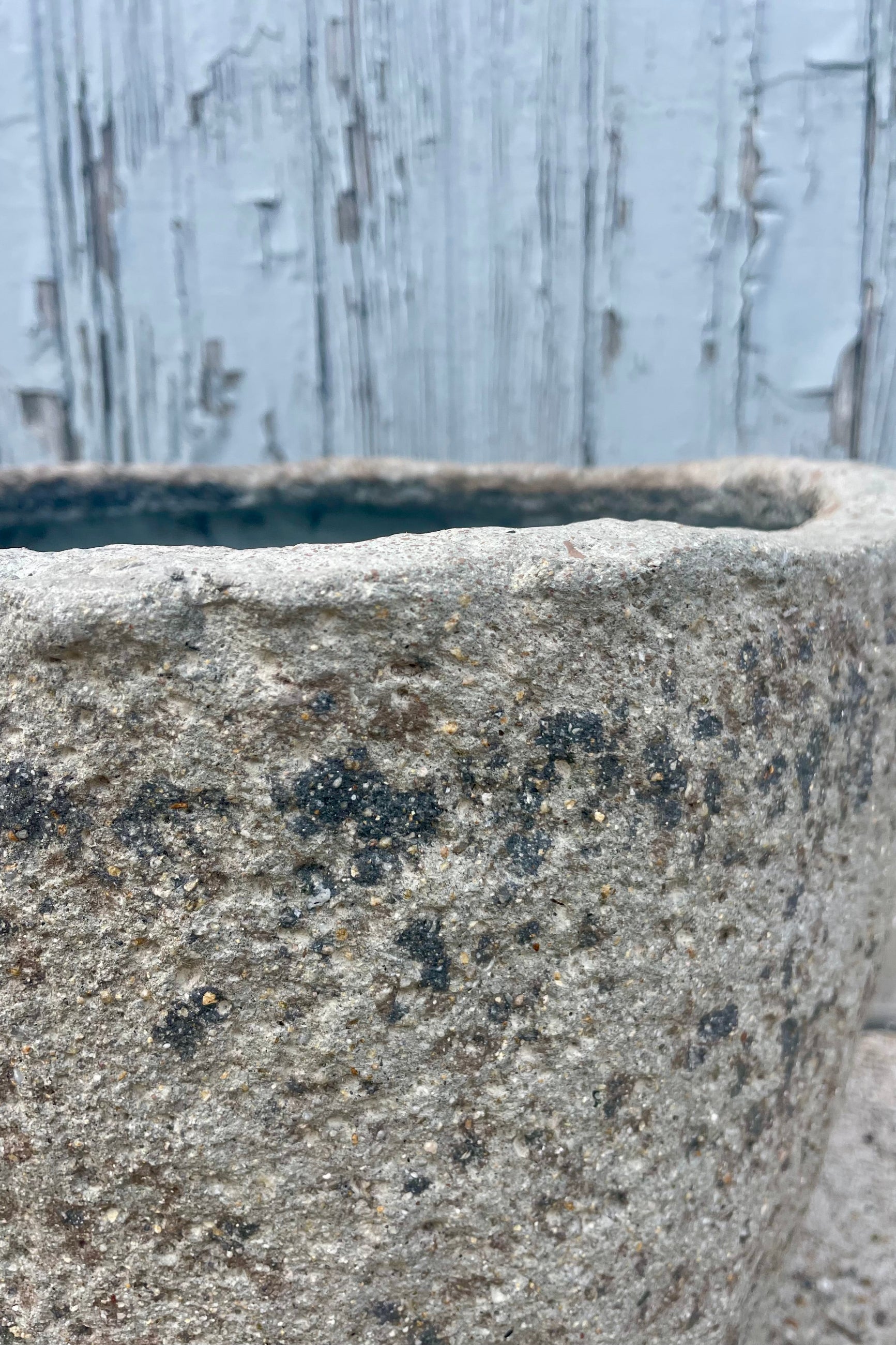 Close photo showing the side and interior opening of a textured gray pot in front of a wooden wall ©Sprout Home