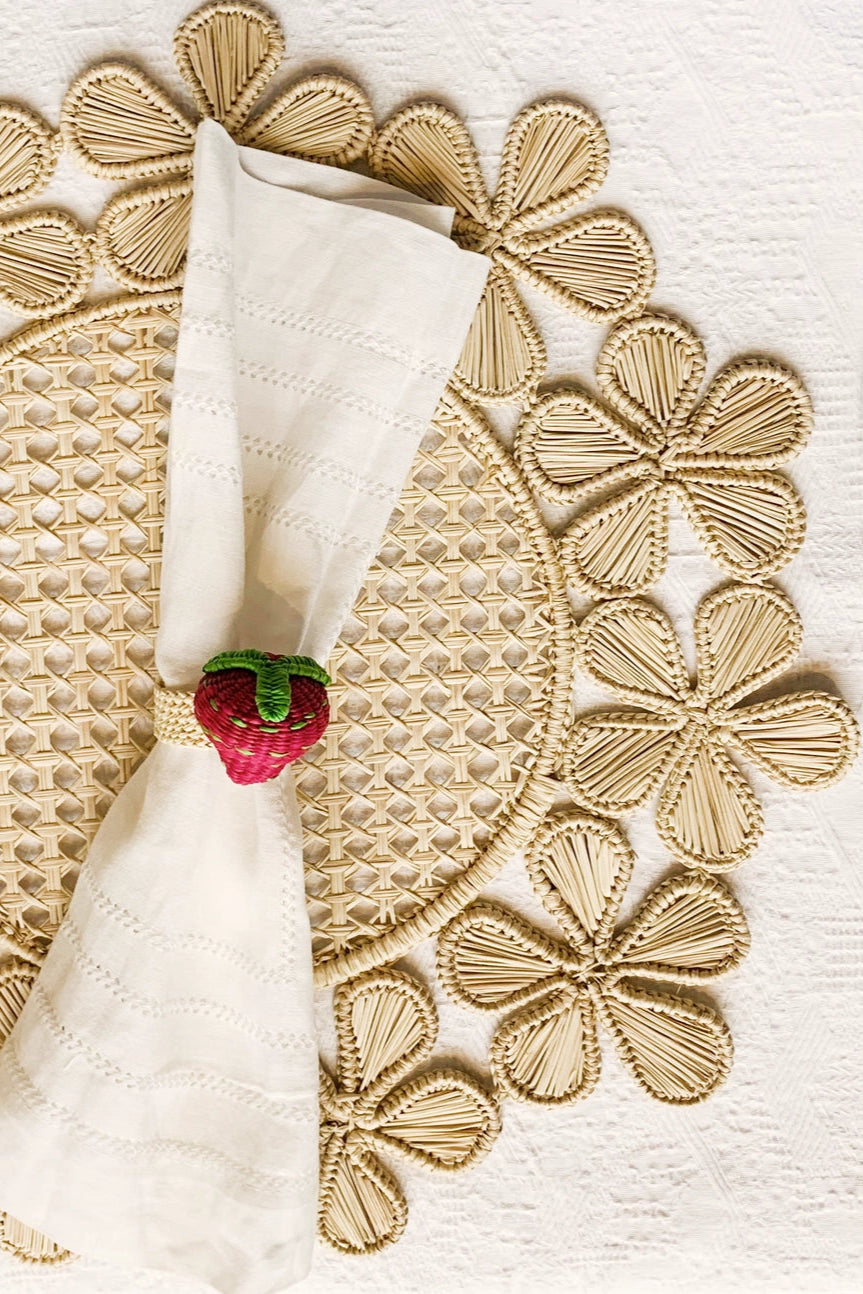 Photo of a neutral place setting of a white napkin with strawberry on a woven placemat on a white background ©Sprout Home