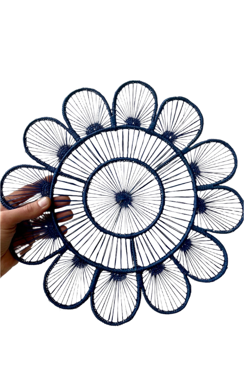 Photo of a hand holding a Lila Placemat Navy of palm fiber and wire. It is shown in front of a white background.