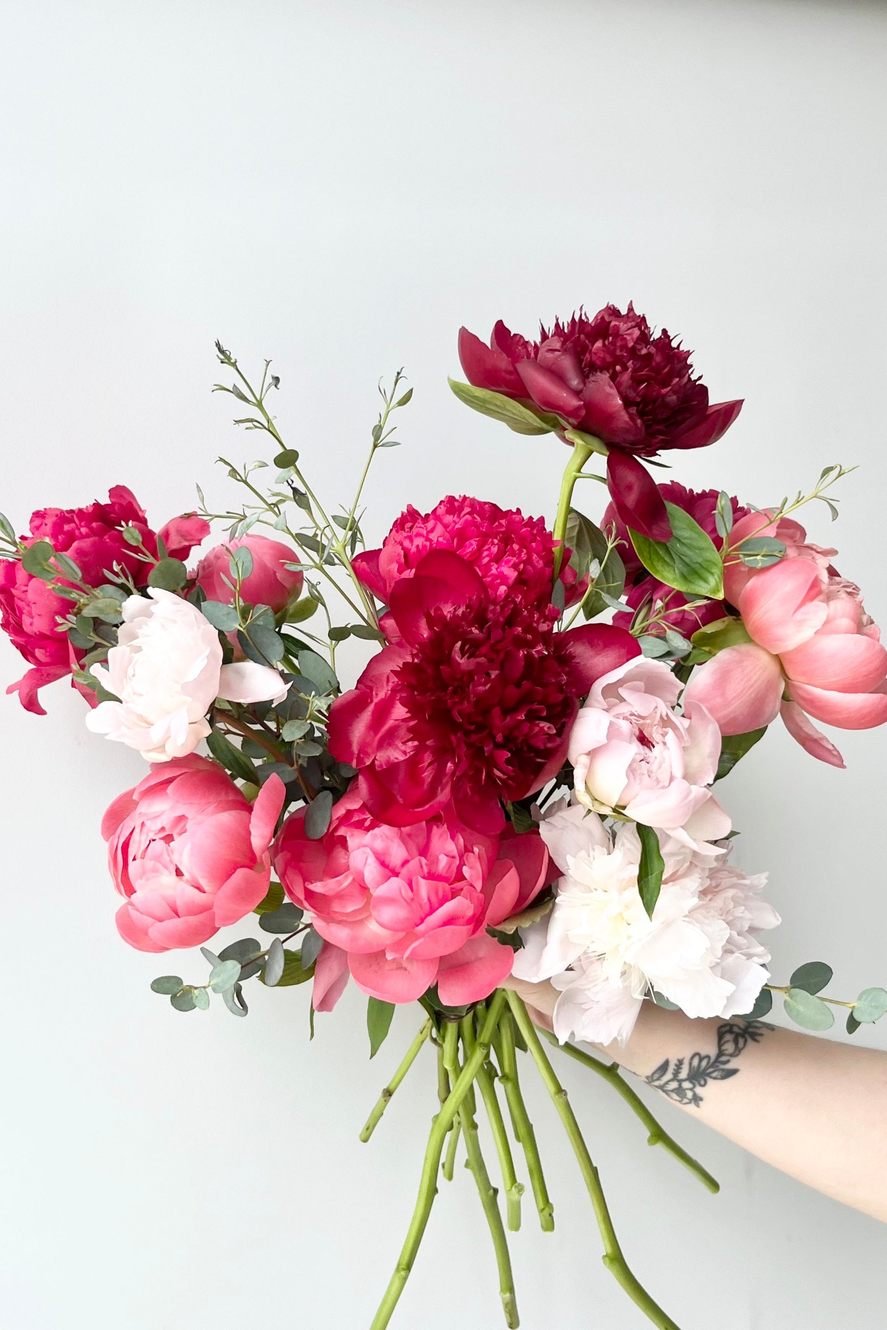 Bouquet of pink, red, and white Paeoniaflowers held by a hand against a light background ©Sprout Home #size_$160