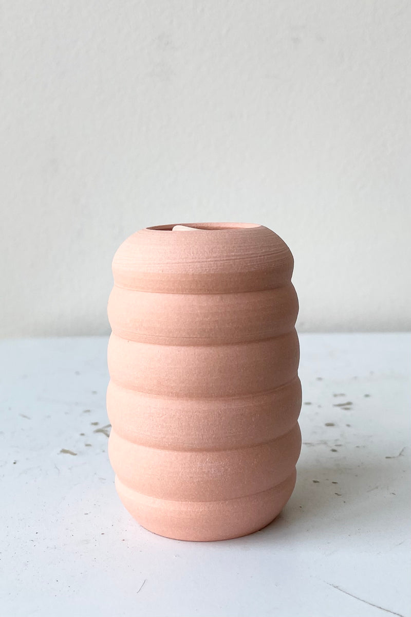 An empty petite Pastel Ribbed vase Peach in front of white. 