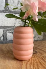 Peite Pastel Peach Ribbed vase on a wood surface in front of white brick. 
