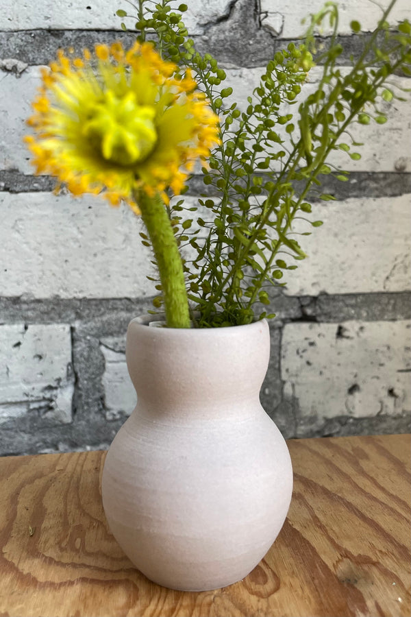 Petite pastel urn vase in lavender with floral and greenery against a white brick wall. 