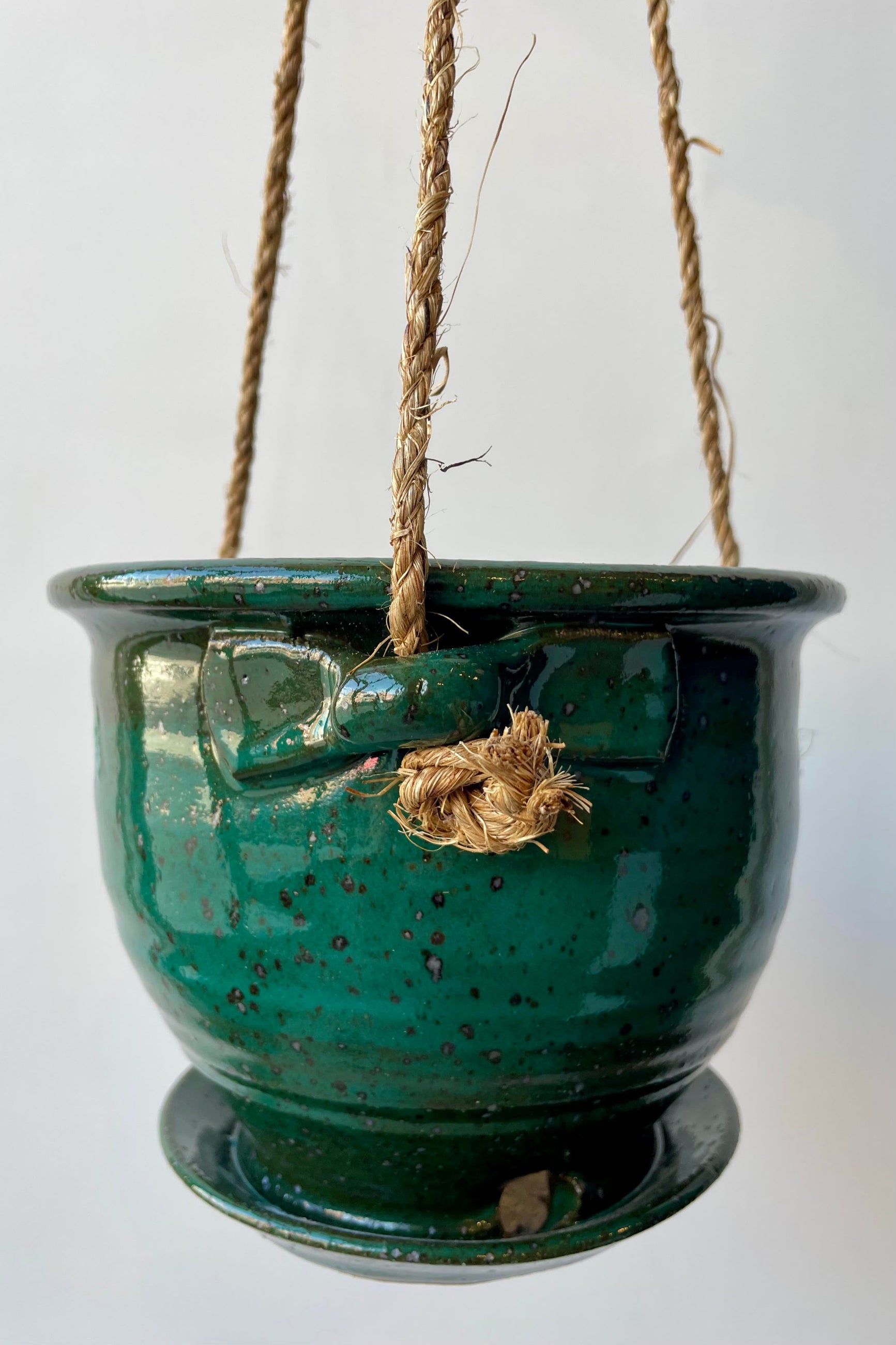 Eight inch clay planter with drainage hole and attached tray in a jade green glaze flecked with silver specks against a white background. The planter has a jute cord attached at three points to hang. ©Sprout Home