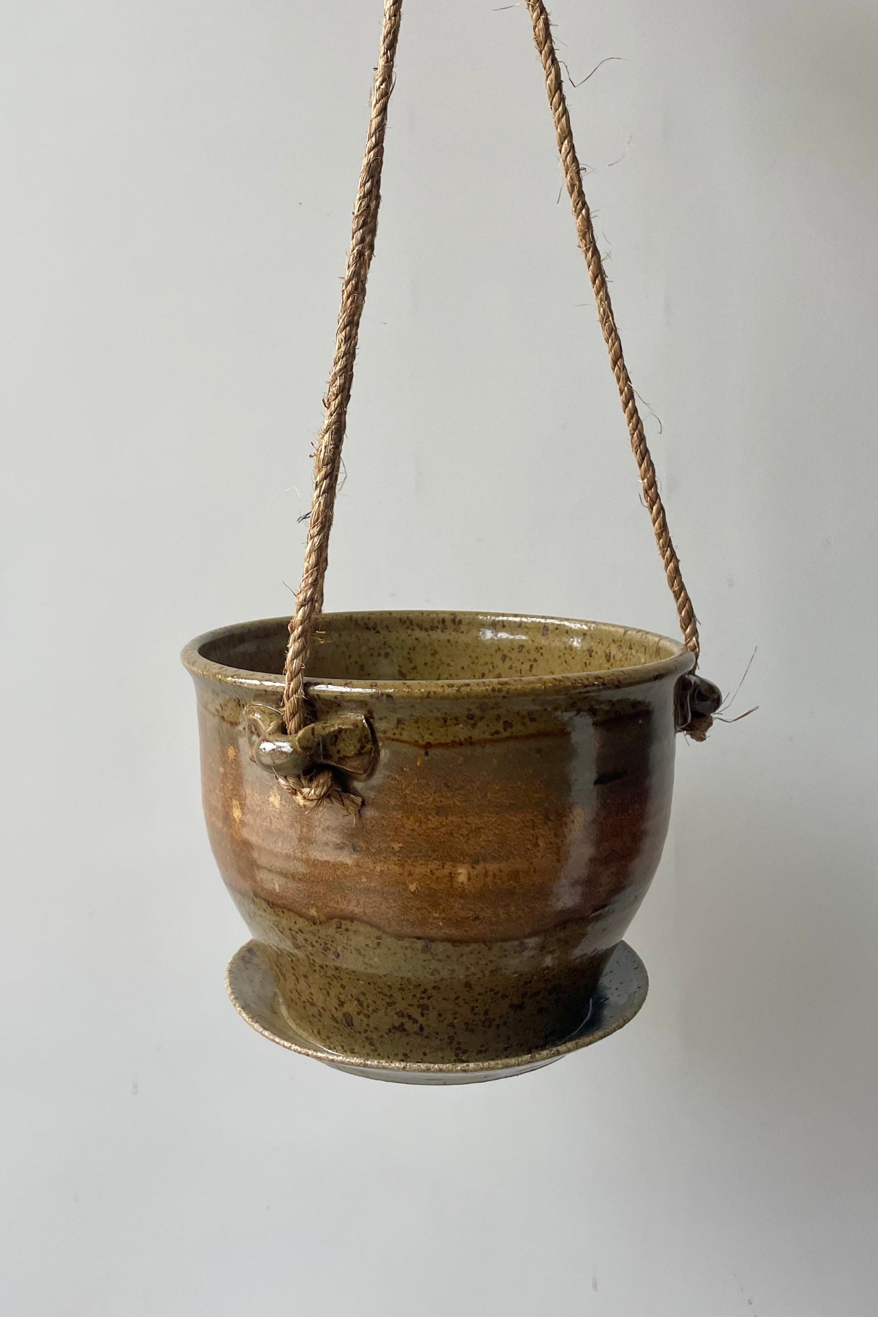 A brown and tan planter with a jute cord hangs in front of a white wall ©Sprout Home
