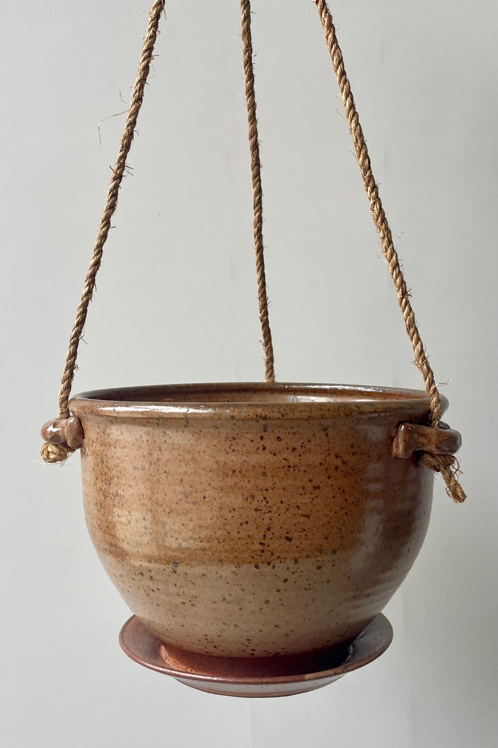 A tan speckled ceramic planter with a jute cord hanging in front of a white wall ©Sprout Home