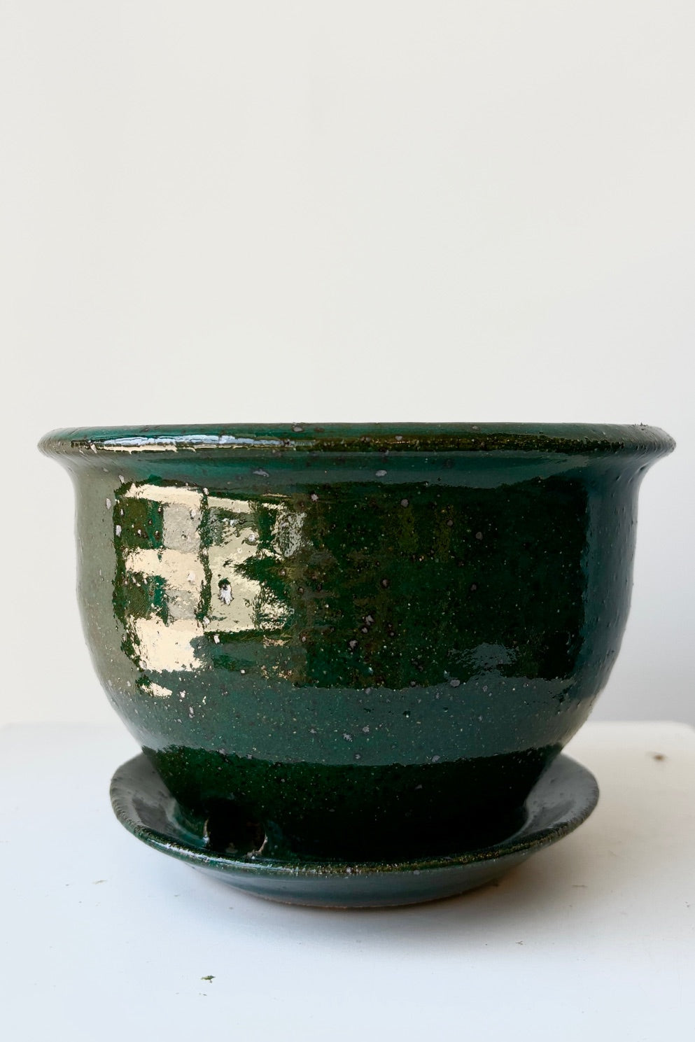 Four inch clay planter with drainage hole and attached tray in a jade green glaze flecked with silver specks against a white background ©Sprout Home