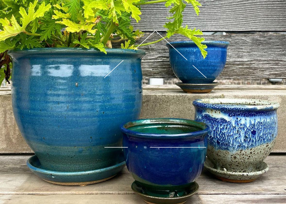 Various sizes of blue and white glazed planters against wood and cement background