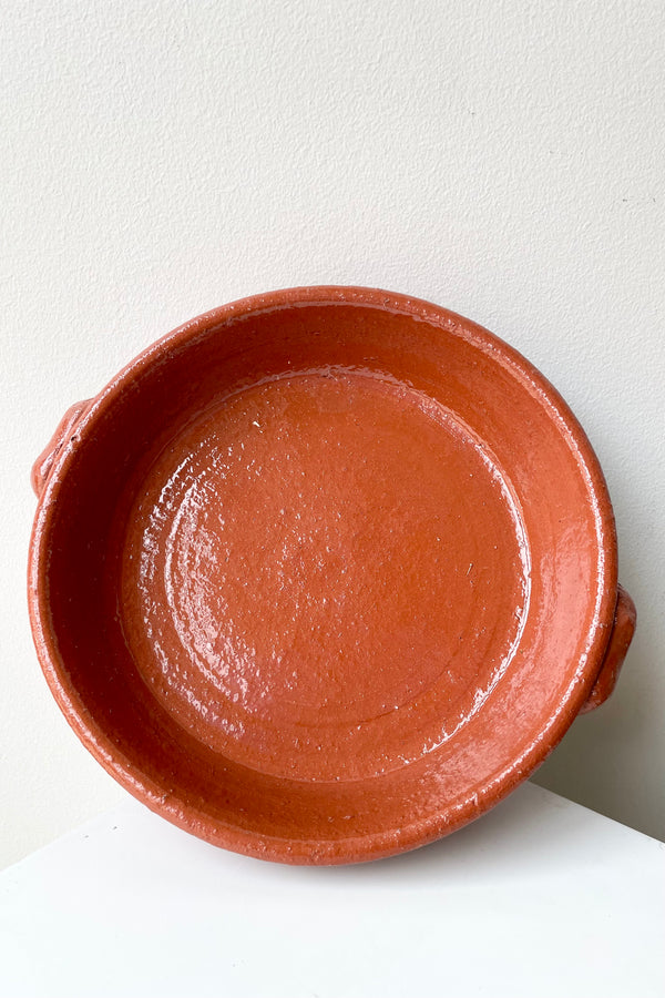 Large Terra cotta roasting dish against a white wall viewed from the top.