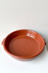 Large terra cotta roasting dish on a white table viewed from above and the side.