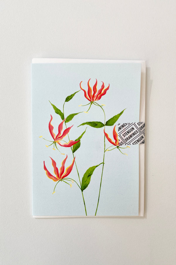 Flame Lily Greeting card by Stengun against a white wall. 