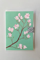 A Magnolia greeting card by Stengun at Sprout Home with its turquoise background and pink flowers. 