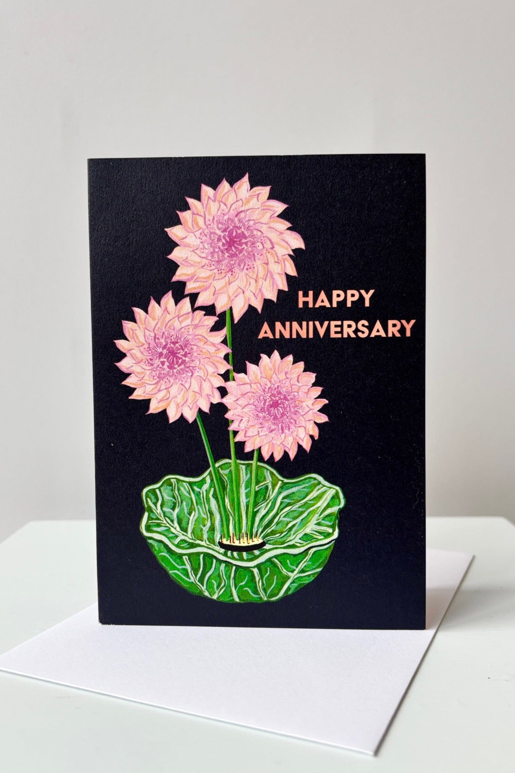 Happy Anniversary greeting card with pink dahlias displayed in a green bowl on a black background shown with envelope ©Sprout Home