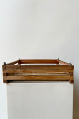 Side view of shallow, square shaped slatted basket with metal rings for string attachment, not included, against white background