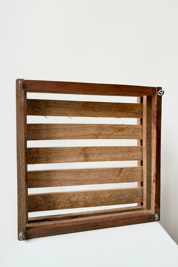 Interior image of shallow, square shaped slatted basket with metal rings for string attachment, not included, against white background