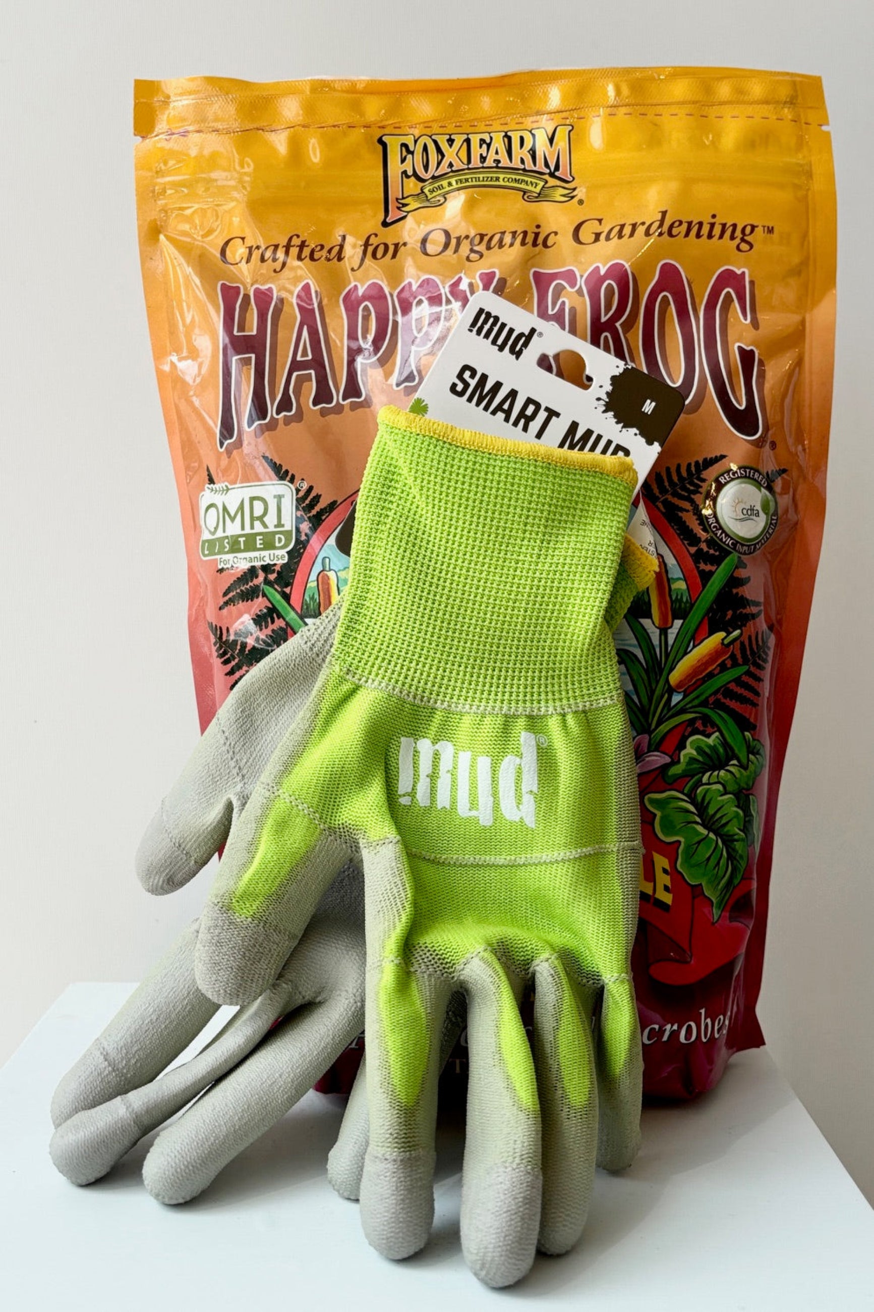 Mud Gloves in apple green displayed with Foxfarm fertilizer against a white wall ©Sprout Home