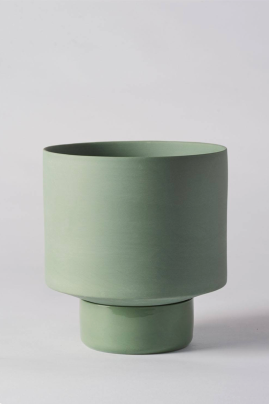 An olive green Collector's Gro pot by Angus & Celeste empty and against a white wall. 