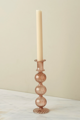 The Nahlia Candlestick in Amaranth color with a taper candle against and off white background. 