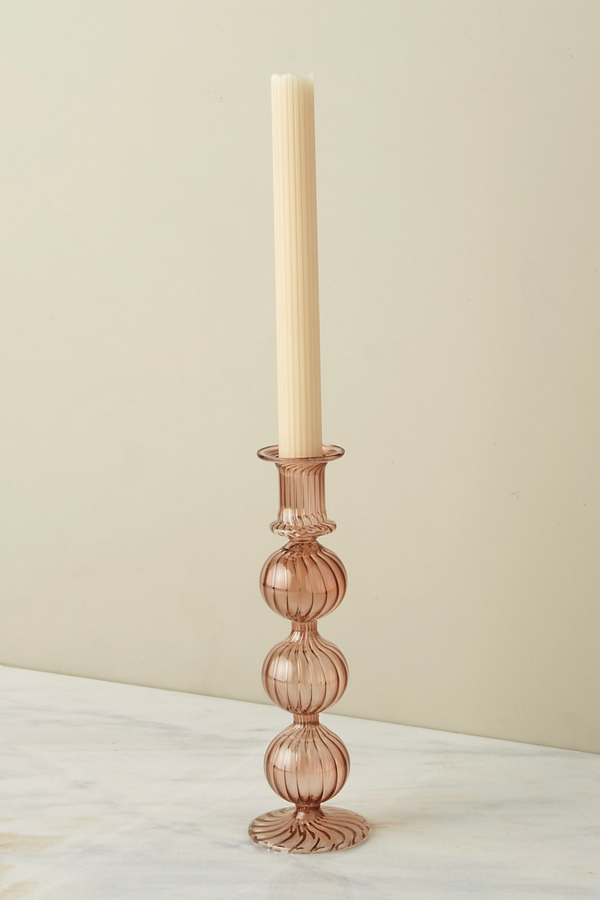 The Nahlia Candlestick in Amaranth color with a taper candle against and off white background. 