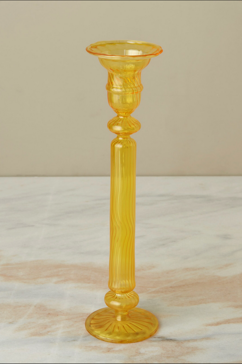 A daffodil Nahlia glass candlestick holder on a gray peach marble counter. 