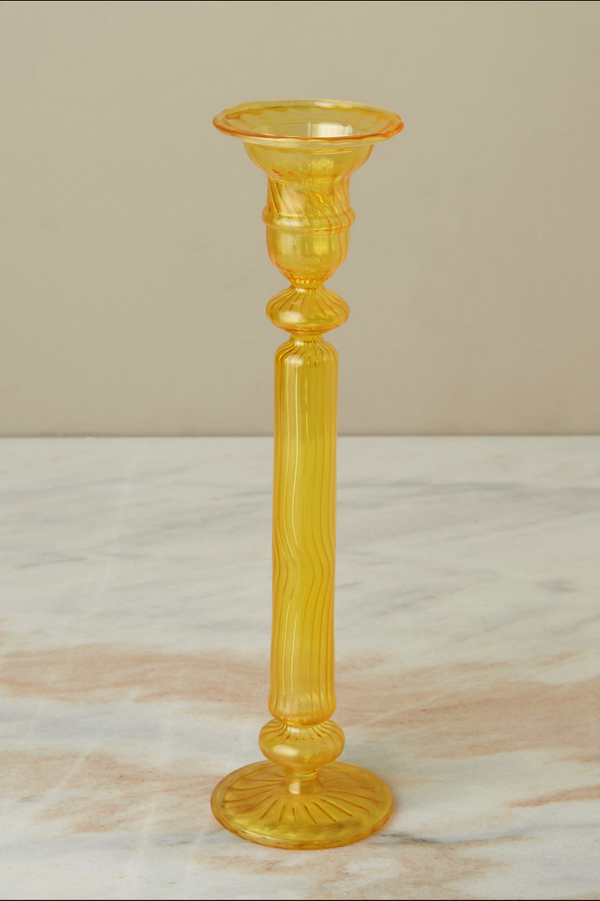 A daffodil Nahlia glass candlestick holder on a gray peach marble counter. 