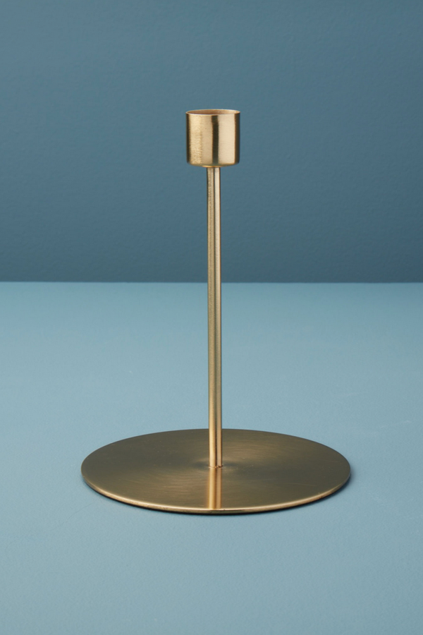 Kent gold tall candlestick holder being shown in front of a contrasting blue. 