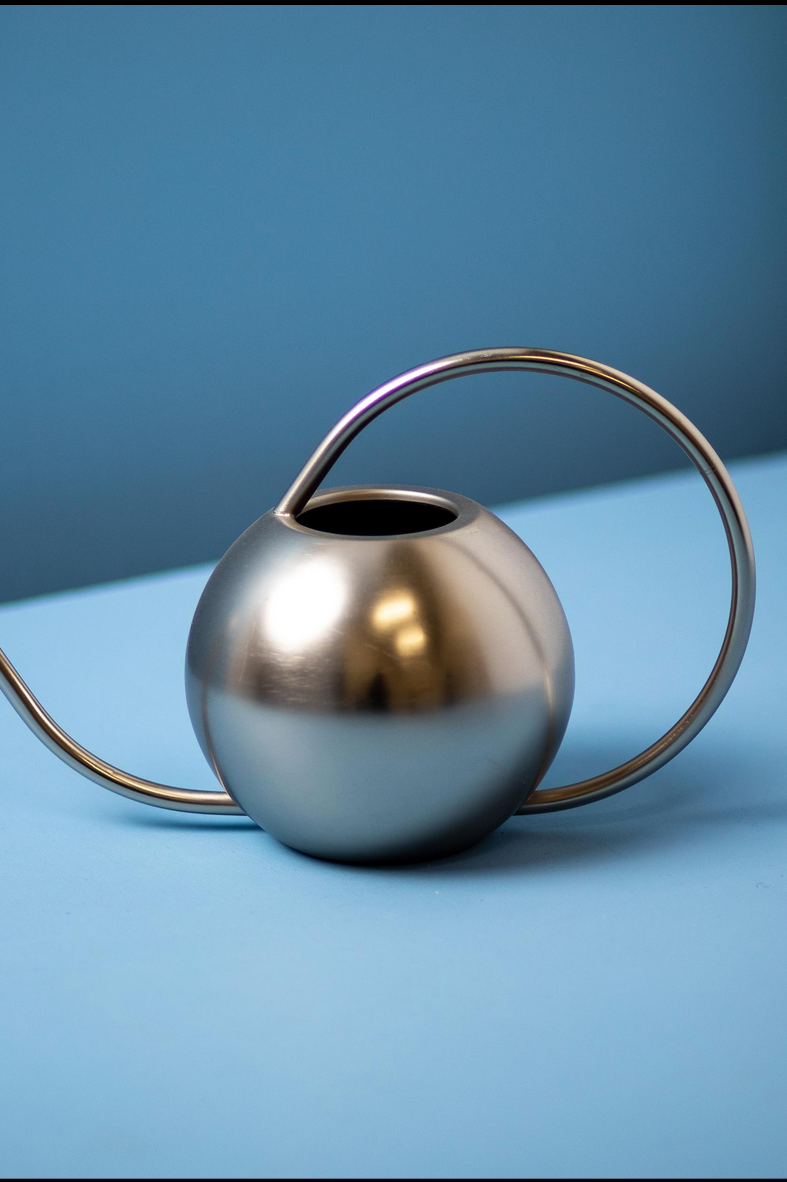 Minto watering can in stainless finish on top of a blue backdrop