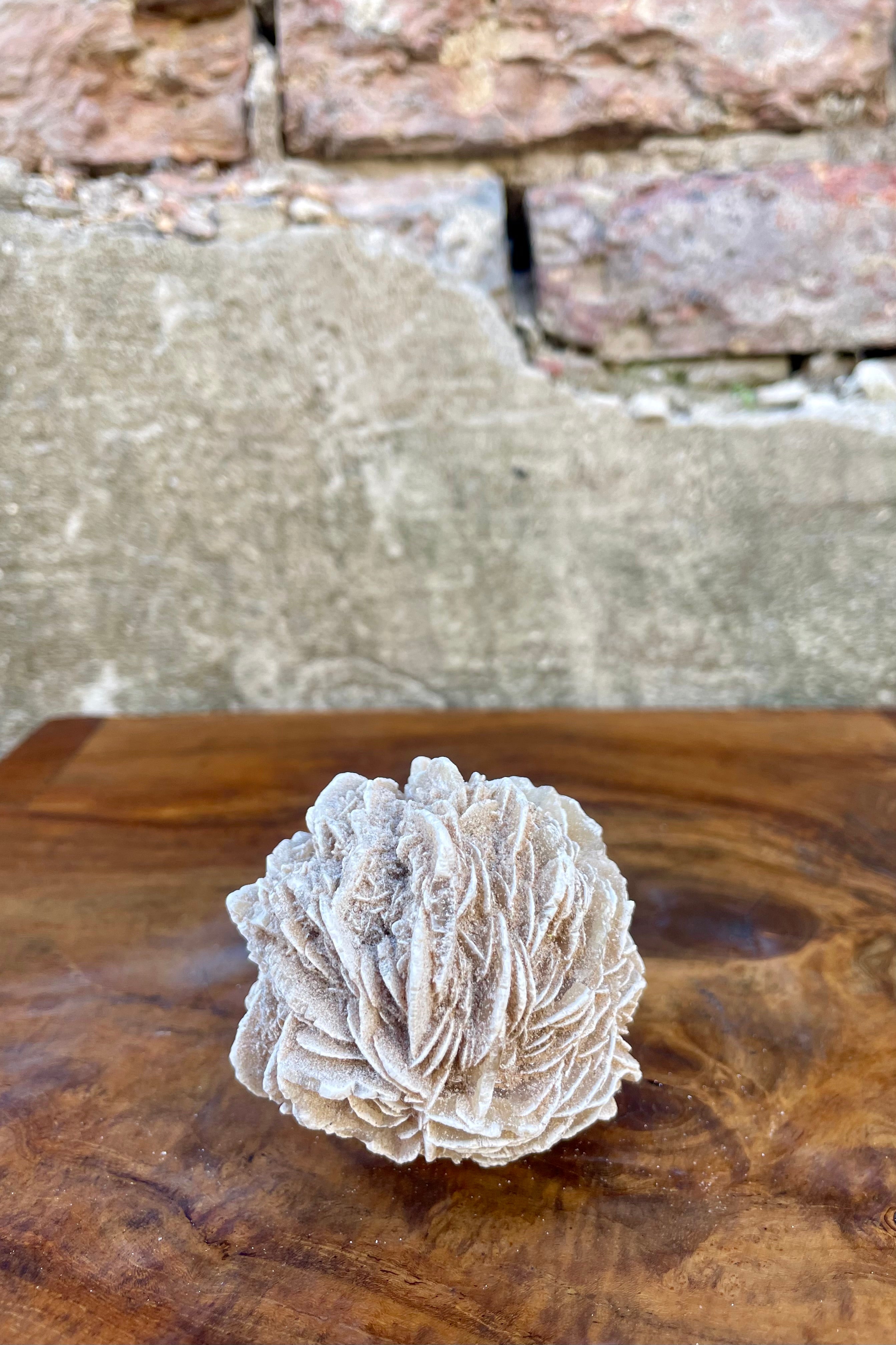 A photo of a selenite specimen on a wood surface in front of a brick wall.