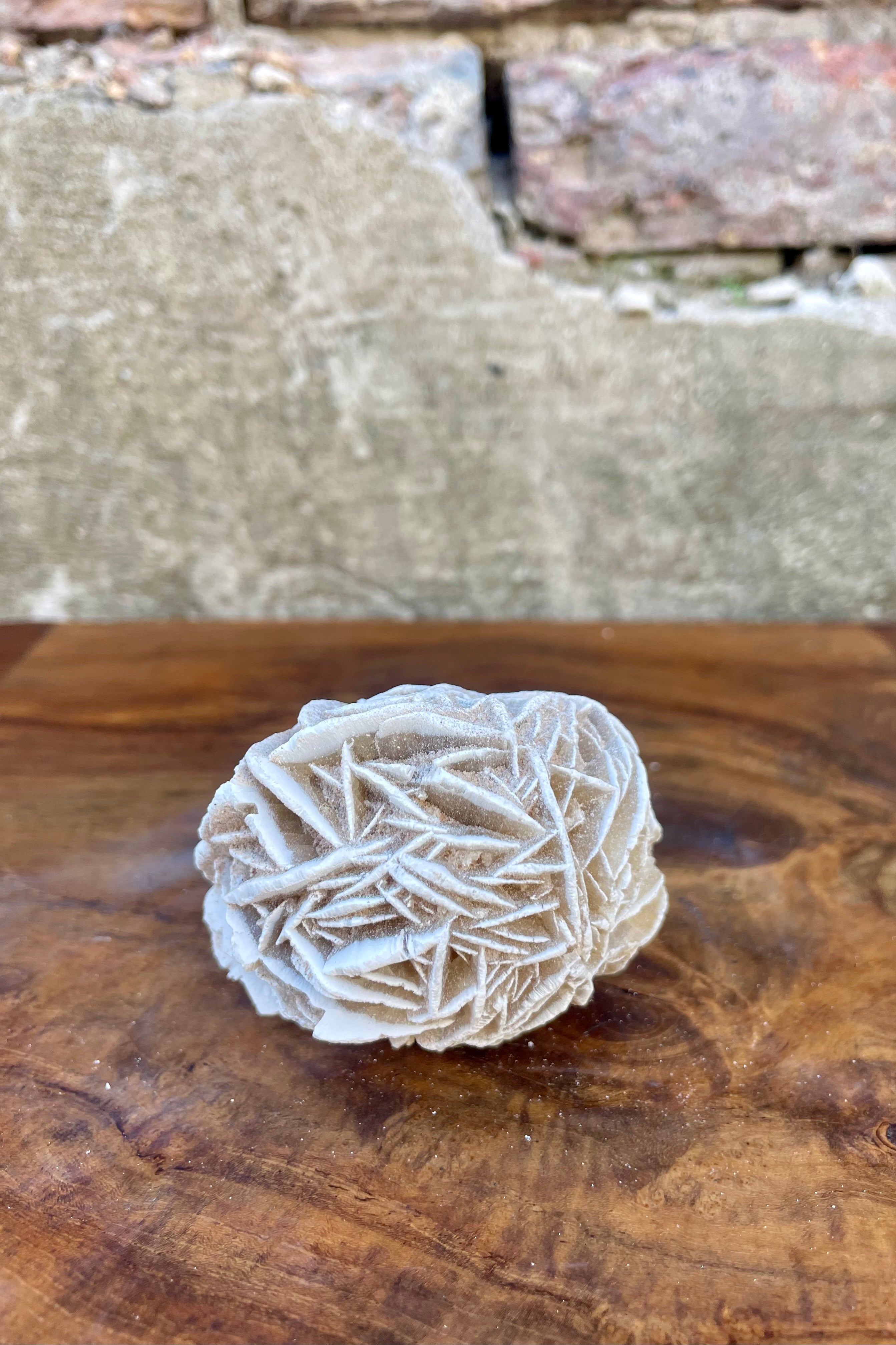 A photo of a selenite specimen on a wood surface in front of a brick wall.