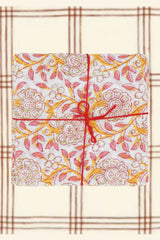 Suzette Frangipanier Jaipur napkins folded in squares, stacked, tied with a red string and on a burgundy and cream plaid 