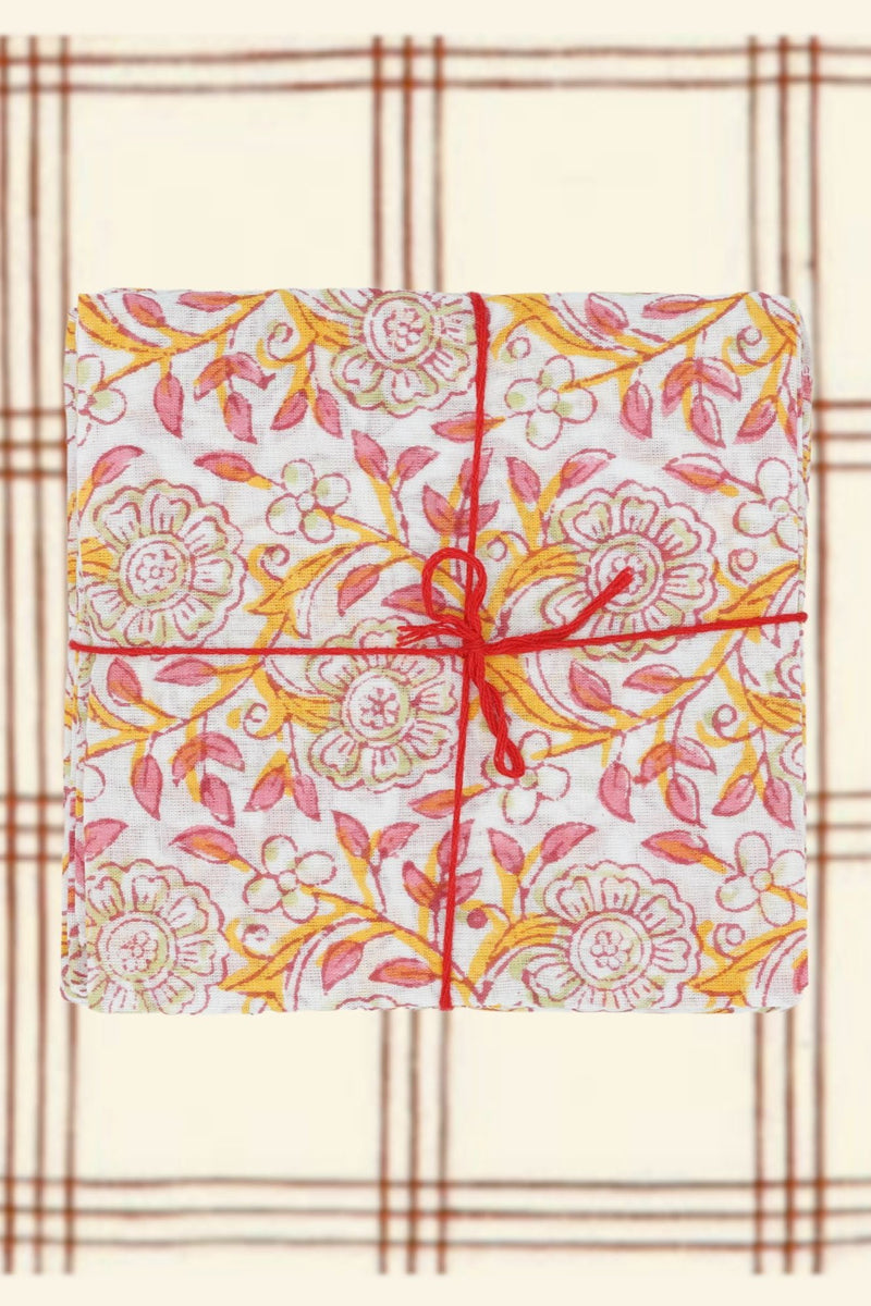 Suzette Frangipanier Jaipur napkins folded in squares, stacked, tied with a red string and on a burgundy and cream plaid 