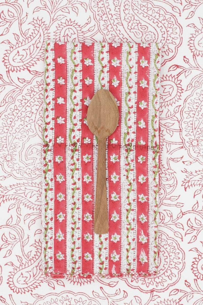 Suzette Cotton Napkin Sweet Pea folded in to a rectangle, wood spoon on top and sitting on a paisley printed background. 