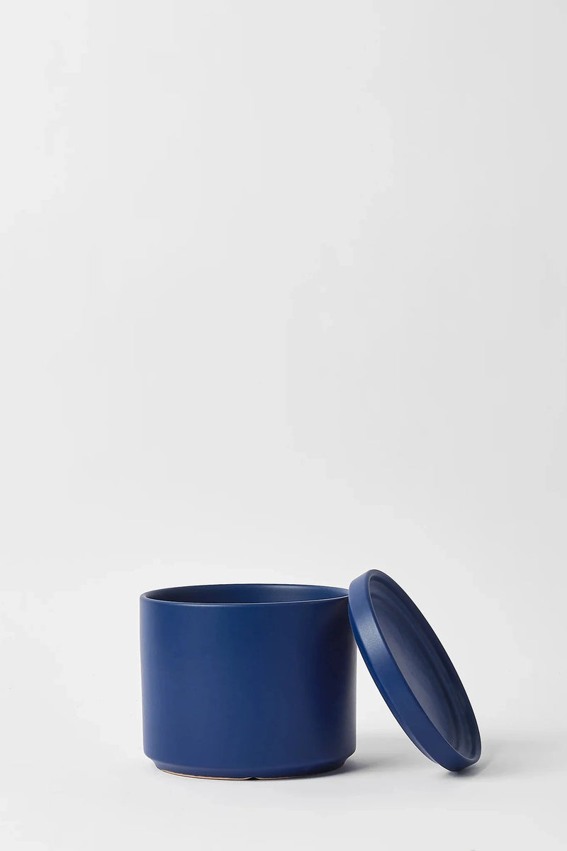 LBE Design Solid Goods Blue Cylinder pot and saucer, with its saucer leaning against the empty pot