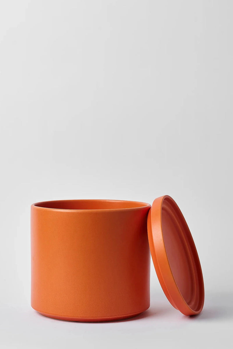 LBE Design Solid Goods Ceramic cylinder planter and saucer in Rust color shown with its saucer leaning against the pot