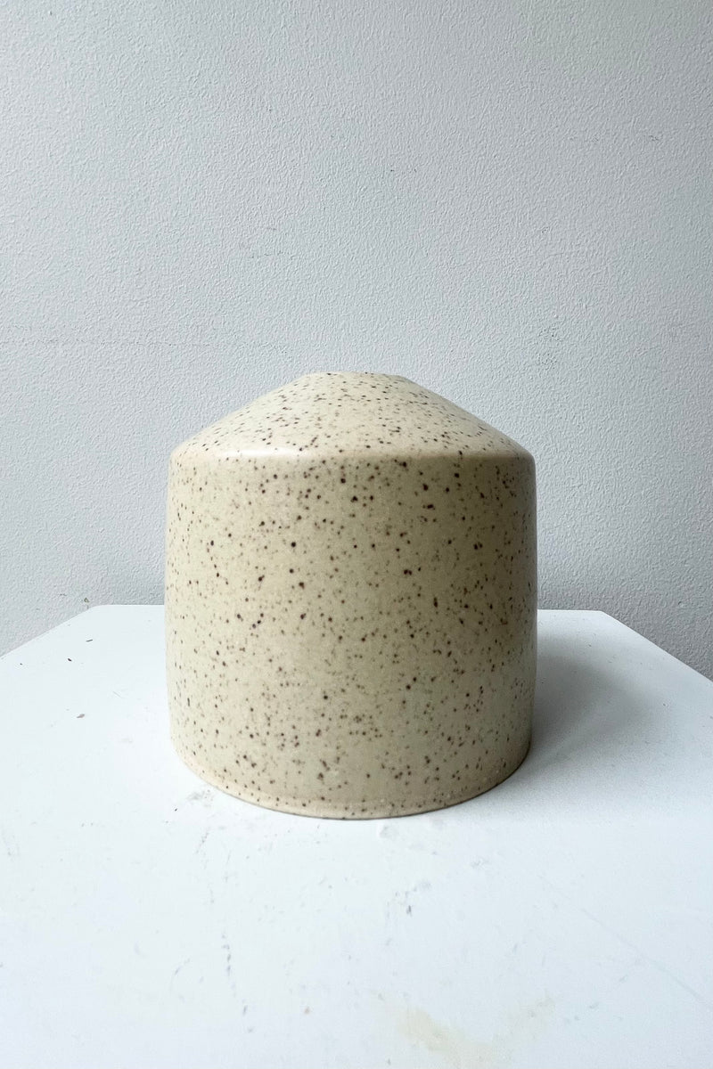 The butter speckle Siros Vase shown from the side against a white wall. 