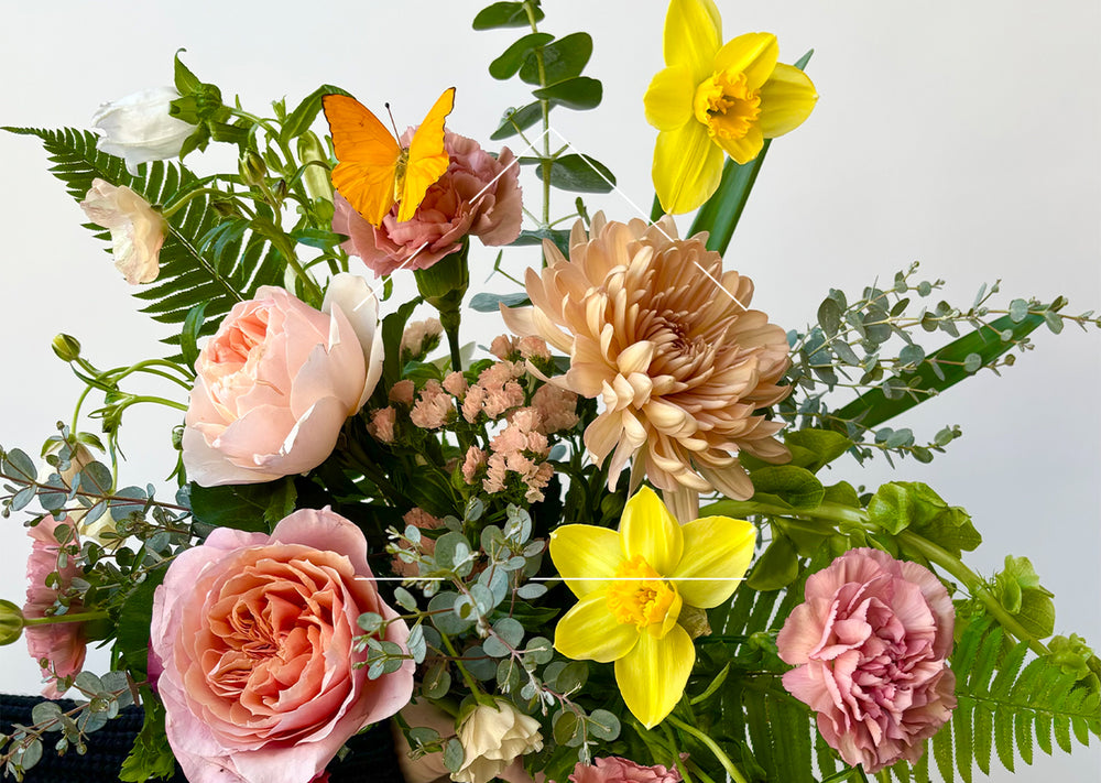 Fresh floral bouquet with pink and peach flowers, yellow daffodils and a yellow butterfly against a white background