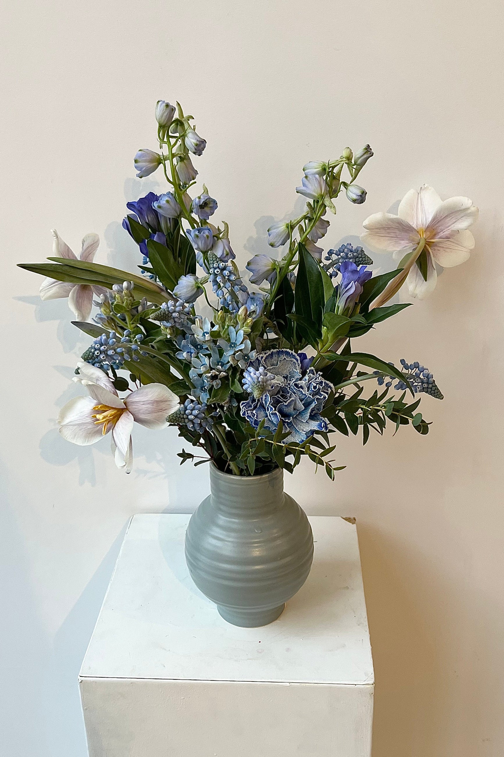 Photo of floral arrangement on a white surface in front of a white wall at Sprout Home. The flowers are various shades of blue, indigo, aqua and teal. ©Sprout Hoe #size_$100