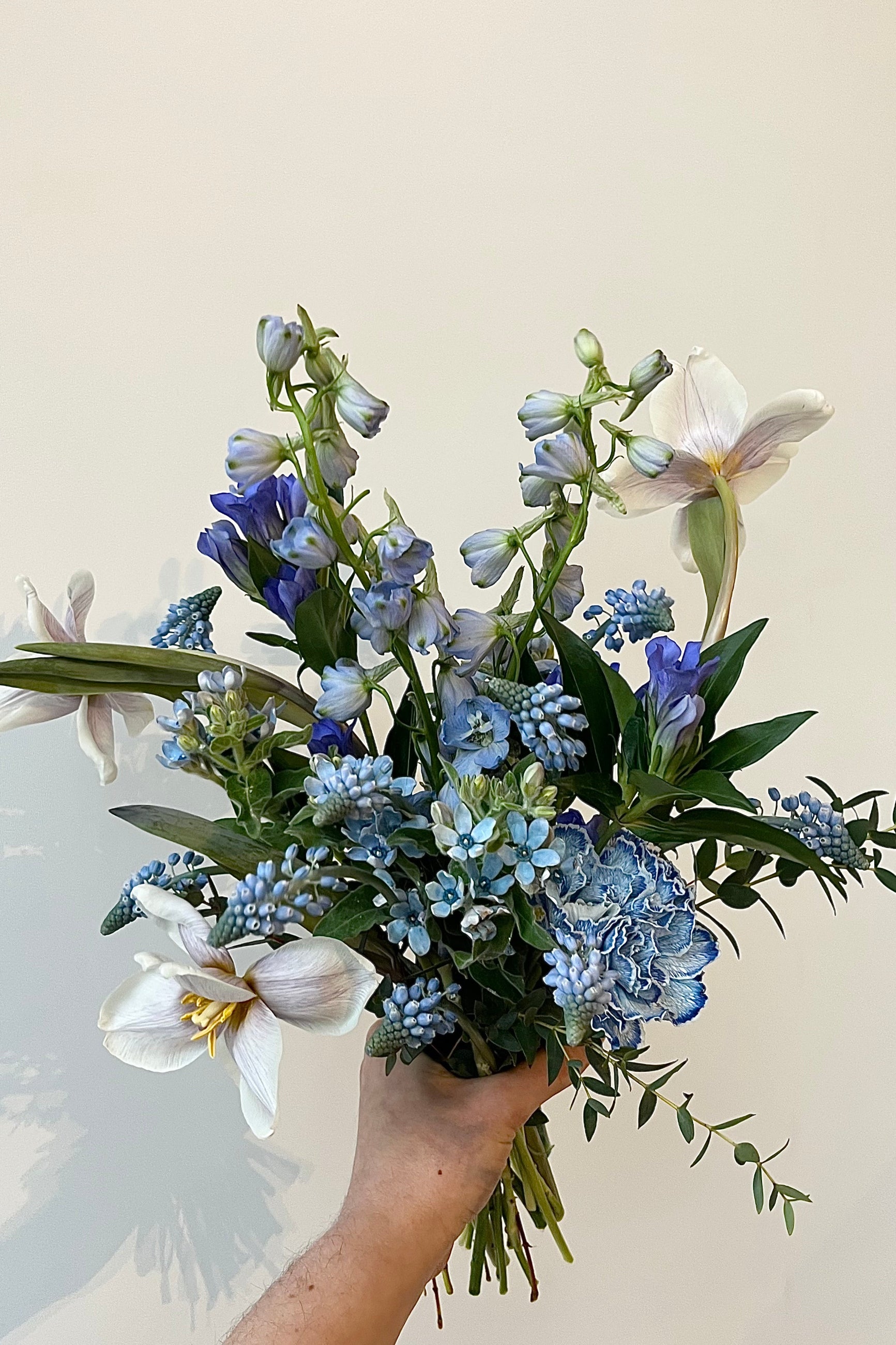Photo of floral arrangement on a white surface in front of a white wall at Sprout Home. The flowers are various shades of blue, indigo, aqua and teal. ©Sprout Home #size_$100