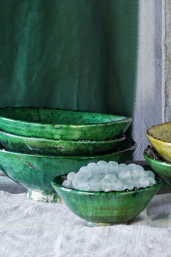 Stacked green Tamegrout bowls with a green drape in the background and a linen color tablecloth. 