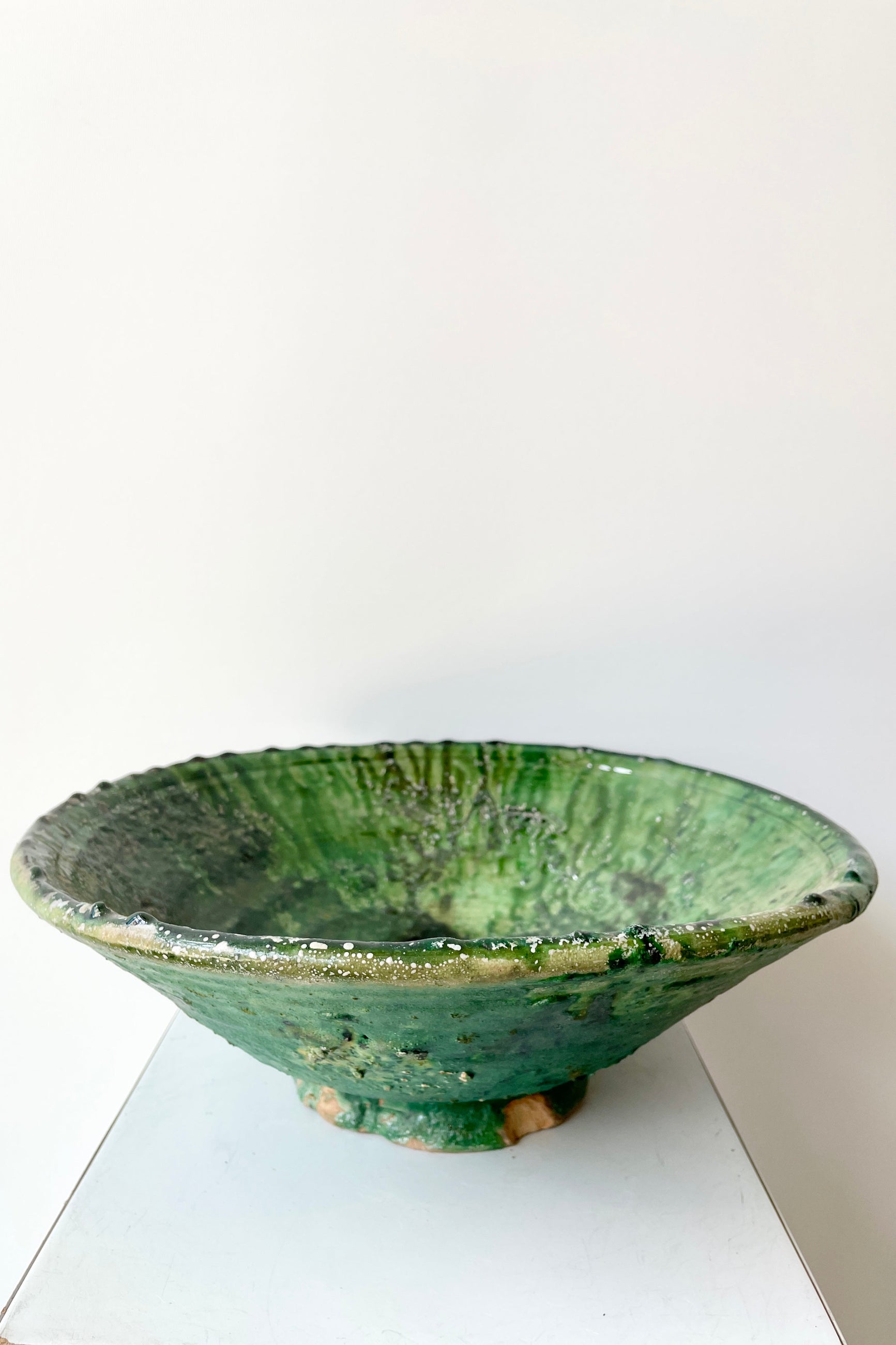 The large tamaegroute green bowl at Sprout Home shown from the side against a white wall.  ©Sprout Home
