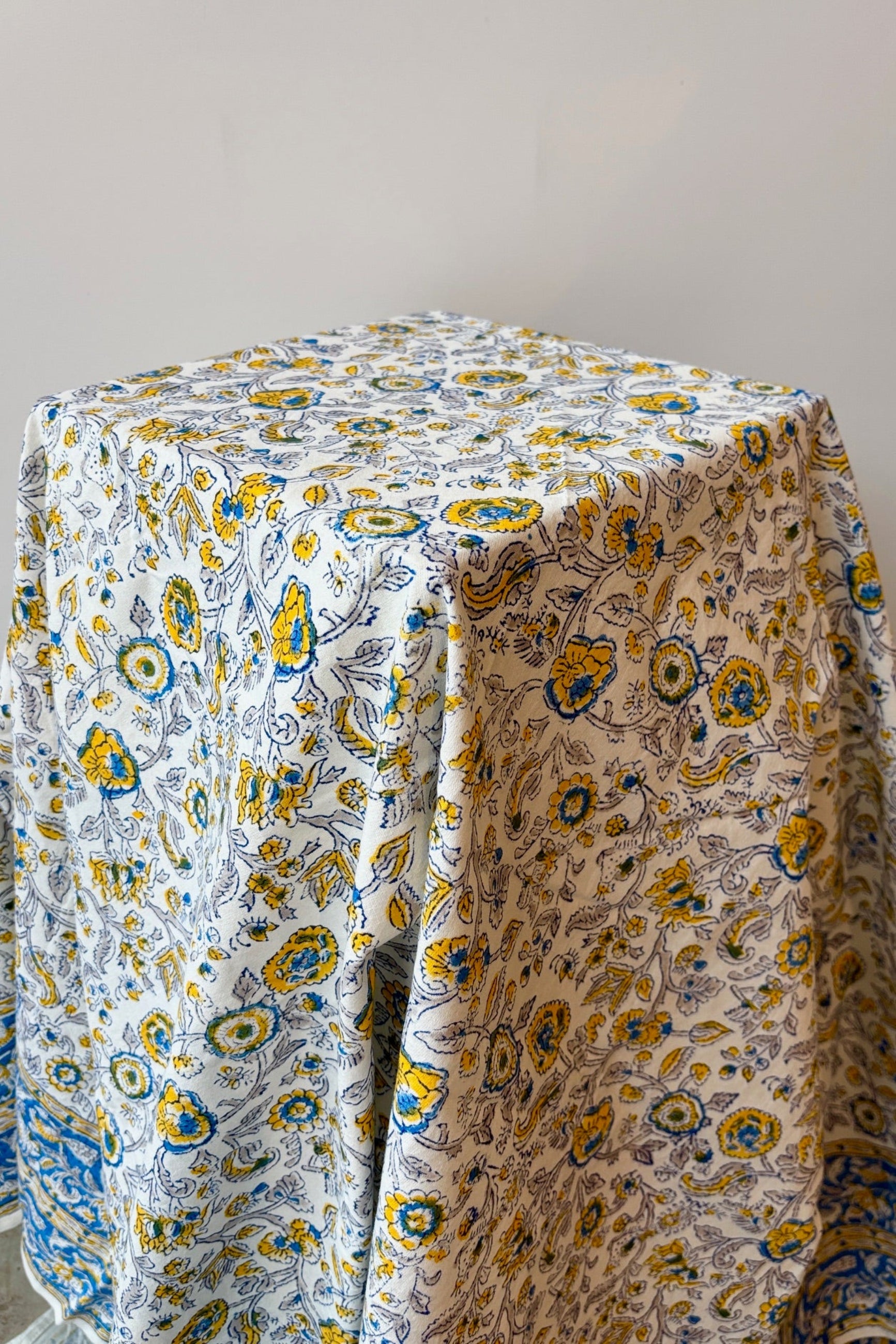 Hand printed, 100% cotton, Provence tablecloth with yellow and blue floral pattern draped on a table against a white wall 